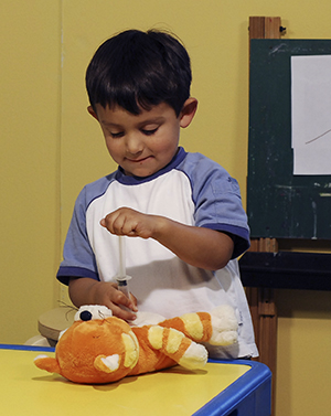 Boy playing with pretend syringe and teddy bear.