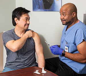 Healthcare provider giving man injection in upper arm in exam room.