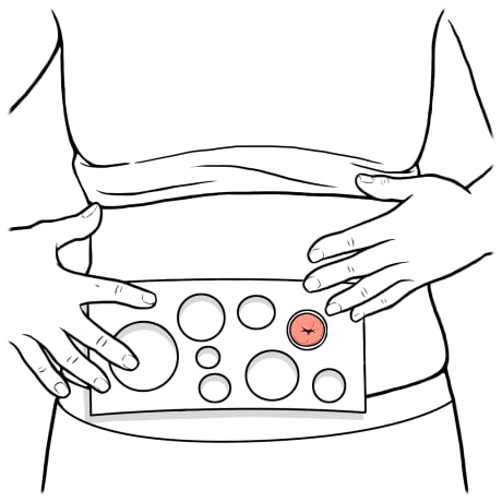 Person holding measuring guide to stoma with one hand and other hand keeping shirt rolled up.