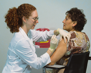 Health care provider preparing to give injection in patient's upper arm.