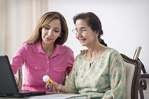Two women looking at medicine bottle and laptop.