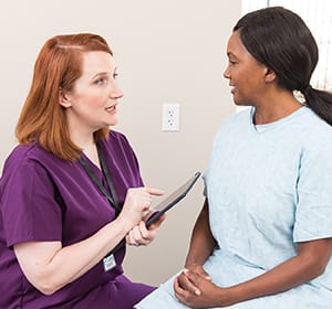 Doctor with digital tablet talking to woman in exam room.