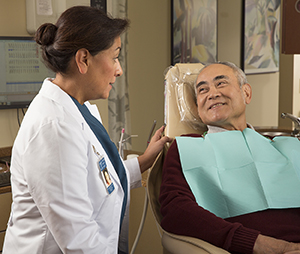 Dental health care provider talking to man in exam chair.
