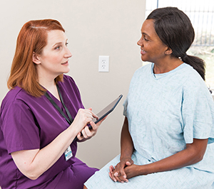 Health care provider with digital tablet talking to woman in exam room.