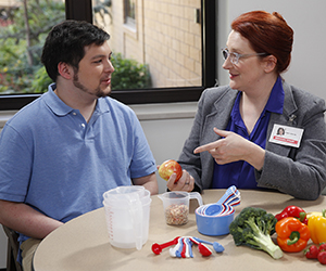 Healthcare provider talking to man. Measuring cups and spoons, fruits and vegetables are on table.