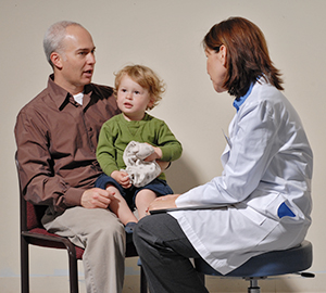 Boy sitting on man's lap while man talks to health care provider.