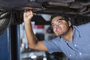 Male mechanic working under lifted car.