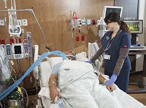 Health care provider caring for intubated person in intensive care unit bed.