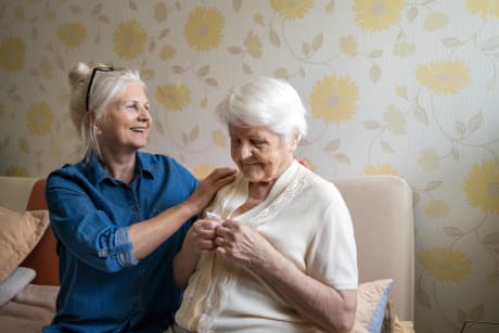 Caregiver helping senior woman dress in her bedroom.